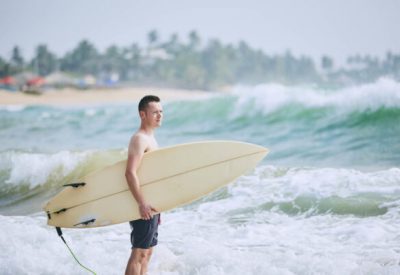 Portrait of surfer. Young man holding surfboard at beach. Tangalle, Sri Lanka.